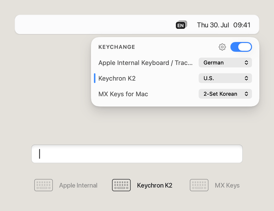 One text field, three keyboards: “Hello!” typed on a Keychron K2 set to U.S., “Grüße!” on the built-in keyboard set to German, and “안녕!” on MX Keys set to 2-Set Korean. The menu bar badge changes from EN to DE to KO as each keyboard is used, and the popover marks whichever one is being typed on.